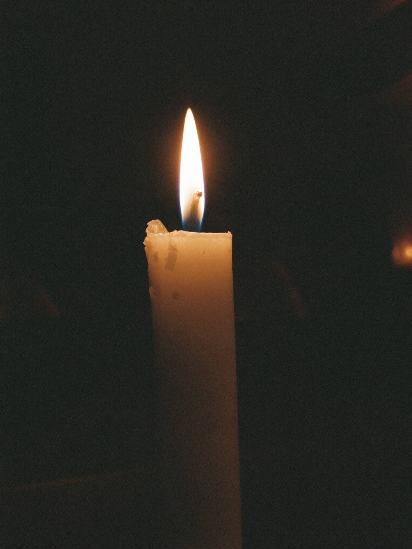 Placeholder — intended image: Single candle flame in a dim chapel, warm glow, dark surround