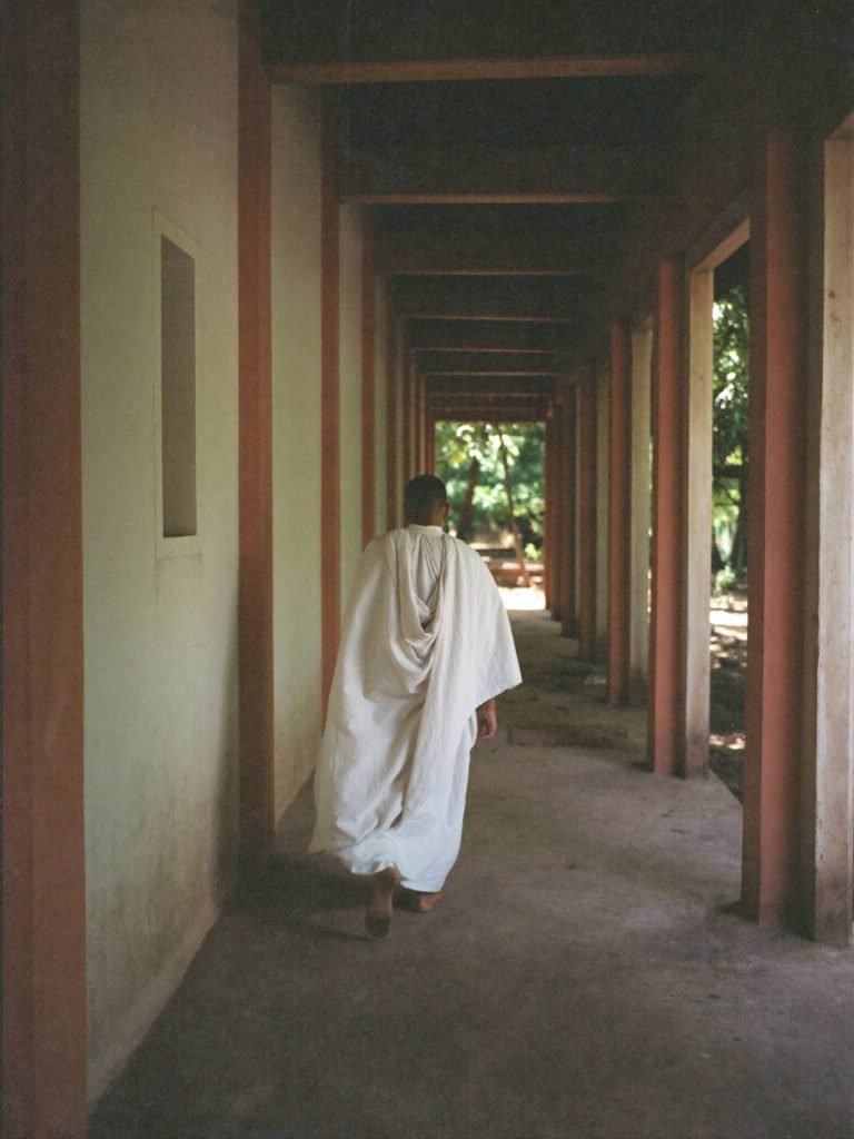 Placeholder — intended image: Monk walking a shaded monastery walkway, soft diffused light, vertical