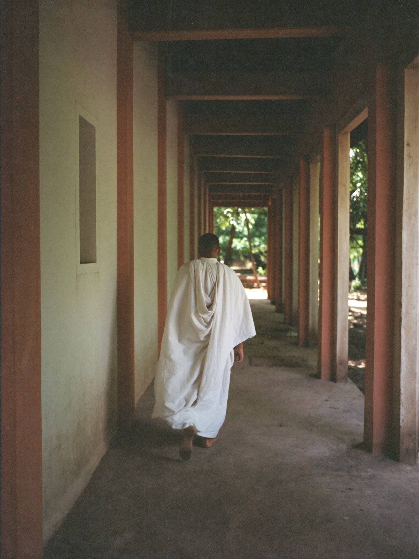 Placeholder — intended image: Monk walking a shaded monastery walkway, soft diffused light, vertical